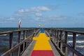 A jetty with a colourful carpet in blue, yellow and red. A blue ocean and sky in the background