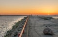 A jetty or pier with silhouetted people with a sunset at sea. Royalty Free Stock Photo