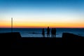 A jetty or pier with silhouetted people with a sunset at sea. Royalty Free Stock Photo