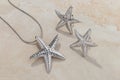 Jewellery set of starfish shape silver pendant necklace and earrings on beige background