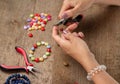 Jewelry making. Making a bracelet of colorful beads. Female hands with a tool on a rough wooden table. Royalty Free Stock Photo