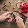 Jewelry making. Making bracelet of colorful beads. Female hands with a tool on a rough wooden table. Royalty Free Stock Photo