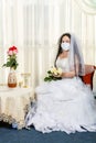 A Jewish bride sits in a synagogue before a chuppa ceremony during a pandemic wearing a medical mask and a bouquet of Royalty Free Stock Photo