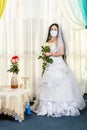 A Jewish bride sits waist-deep in a synagogue at a table with flowers before a chuppa ceremony during a pandemic Royalty Free Stock Photo