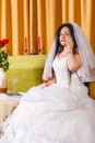 A Jewish bride in a white wedding dress with a veil sits at a table with flowers and speaks on the phone before the Royalty Free Stock Photo