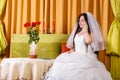 A Jewish bride in a white wedding dress with a veil sits at a table with flowers and speaks on the phone before the Royalty Free Stock Photo