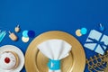 Jewish holiday Hanukkah border background with golden plate, traditional donuts, menorah and gift box on blue tabletop. Top view, Royalty Free Stock Photo