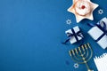 Jewish holiday Hanukkah concept. Flat lay composition with traditional jelly donut, menorah, candles and gift boxes on blue Royalty Free Stock Photo