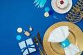 Jewish holiday Hanukkah concept with golden plate, traditional donuts, menorah and gift box on blue background. Top view, flat lay