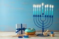 Jewish holiday Hanukkah concept with menorah, traditional donuts and gift box on wooden table Royalty Free Stock Photo