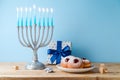 Jewish holiday Hanukkah concept with menorah, traditional donuts and gift box on wooden table Royalty Free Stock Photo