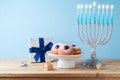 Jewish holiday Hanukkah concept with menorah, traditional donuts and gift box on wooden table Royalty Free Stock Photo