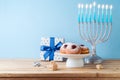 Jewish holiday Hanukkah concept with menorah, traditional donuts and gift box on wooden table Royalty Free Stock Photo