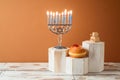 Jewish holiday Hanukkah creative concept with menorah and traditional donuts on podium on wooden table Royalty Free Stock Photo