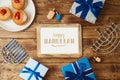 Jewish holiday Hanukkah greeting card with photo frame, traditional donuts, menorah and gift box on wooden background