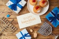 Jewish holiday Hanukkah greeting card with traditional donuts, menorah and gift box on wooden background