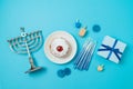 Jewish holiday Hanukkah top view composition with menorah, traditional donuts and gift box on blue background. Flat lay