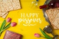 Jewish holiday Passover Pesah celebration with matzoh, tulip flowers and wine bottle on yellow wooden background.