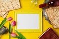 Jewish holiday Passover Pesah celebration with photo frame, matzoh and wine bottle on yellow wooden background.