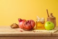 Jewish holiday Rosh Hashana concept with honey jar, apple and pomegranate on wooden table over yellow background Royalty Free Stock Photo