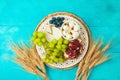 Jewish holiday Shavuot festive table setting with cheese, fruits and wheat ears on wooden blue table background. Top view from