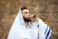 Jewish man blowing shofar on Rosh Hashanah. Wearing tallit with words Blessed Are You, Lord Our God, King Of The Universe