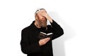 Jewish man holding Siddur covering eyes with hand on white background. Bearded Jew hasid with sidelocks in white kippah