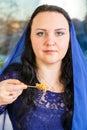 A Jewish woman with her head covered in a blue cape at the Passover Seder table eats haroset.