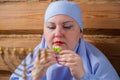 A Jewish woman with her head covered in blue at the Pesach Seder table eats matzo and maror