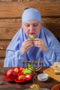 A Jewish woman with her head covered eats matzah and maror at the Pesach Seder table