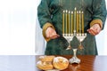 A Jewish woman with her head covered stands at the festive table and Hanukkah lamp.