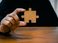 A jigsaw puzzle in businessman hand. Man in black shirt showing empty piece of important jigsaw puzzle on wood desk. Business Royalty Free Stock Photo