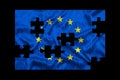 A jigsaw puzzle with a print of the flag of European Union, some pieces of the puzzle are scattered or disconnected. Black