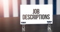 Job Descriptions sign on paper on dark desk in sunlight. Blue and white background Royalty Free Stock Photo