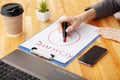 Job search. Female hand writes resume with lipstick on white sheet of paper. Wooden office desk with laptop, smartphone