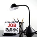 JOB SEARCHING text on notebook with pen and table lamp on the black background