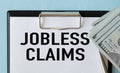 Jobless claims text on white paper from a notepad and dollars on blue background