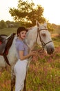 Jockey young girl petting and hugging white horse in evening sunset. Sun flare