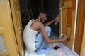 Jodhpur, rajasthan, india, 20th September 2020: Indian male adult painting the entrance door wearing jeans and vest while sitting