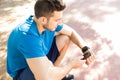 Jogger Syncing Smart Watch With Smartphone While Sitting In Park