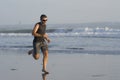 Jogging Summer workout - young attractive and fit runner man training on beautiful beach running barefoot free and happy by the Royalty Free Stock Photo