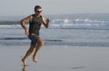 Jogging Summer workout - young attractive and fit runner man training on beautiful beach running barefoot free and happy by the Royalty Free Stock Photo