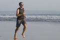 Jogging Summer workout - young attractive and fit runner man training on beautiful beach running barefoot free and happy by the Royalty Free Stock Photo