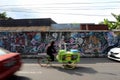 A rickshaw driver rides past graffiti and traffic on Tirtodipuran Street in Jogyakarta