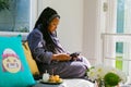 Young African woman in bath robe watching streaming service on tablet computer at spa resort