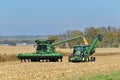 John Deer tractor pulling a Brent Avalanche grain cart while corn is being loaded from a John Deere harvester