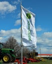 John Deere banner flag in front of agricultural machineries by the local dealership of the american company.