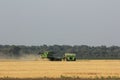 John Deere Combine cutting wheat in a farm field by a tractor and trailer for dumping wheat on the move when cutting in Kansas.