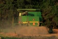 John Deere combine cutting wheat with tree`s and dust coming out of the combine out in the country in Kansas.