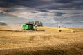 John Deere Combine harvesting with dust trail passing round hay bales on the Canadian Prairies. Royalty Free Stock Photo